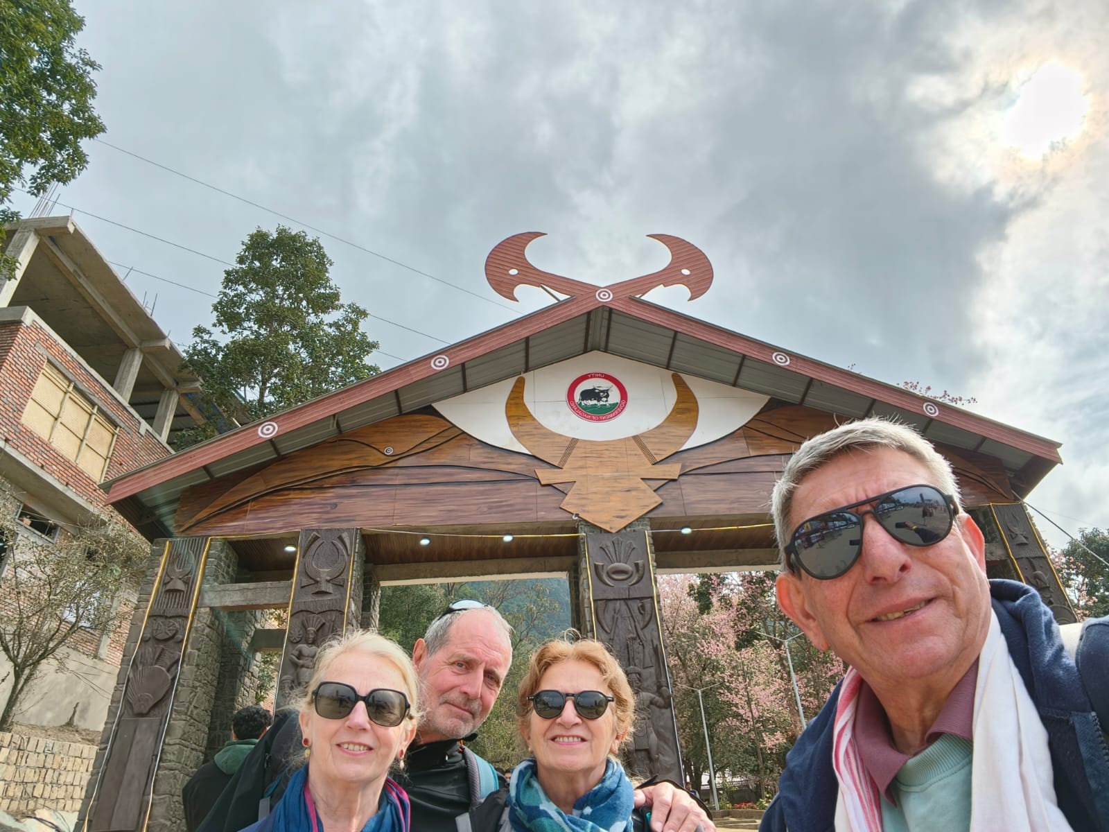 Four travellers taking a selfie beneath the carved mithun-horn gateway at Kisama Heritage Village, Nagaland