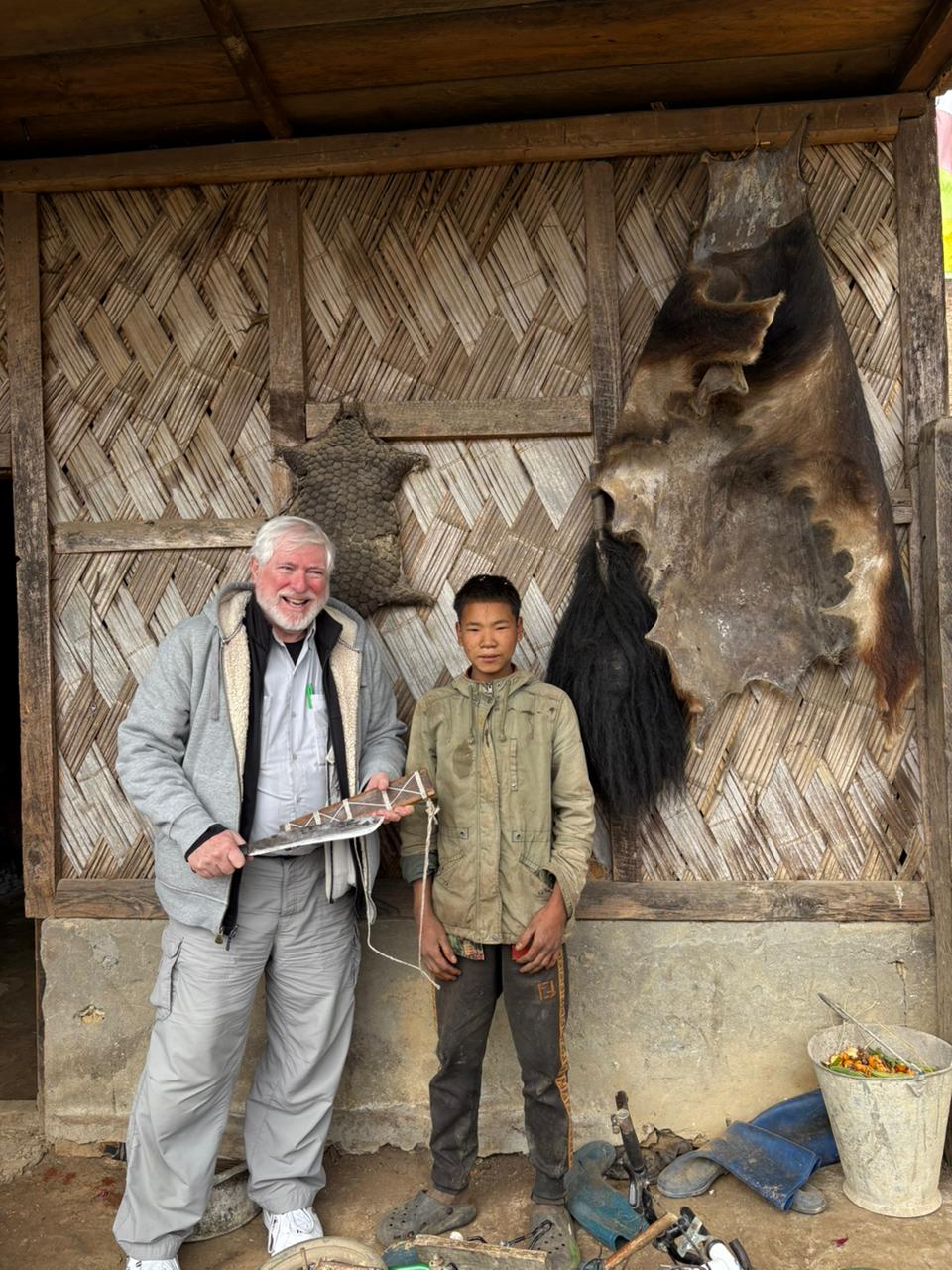George Lowe with a young villager in front of a bamboo house hung with animal hides in Arunachal Pradesh