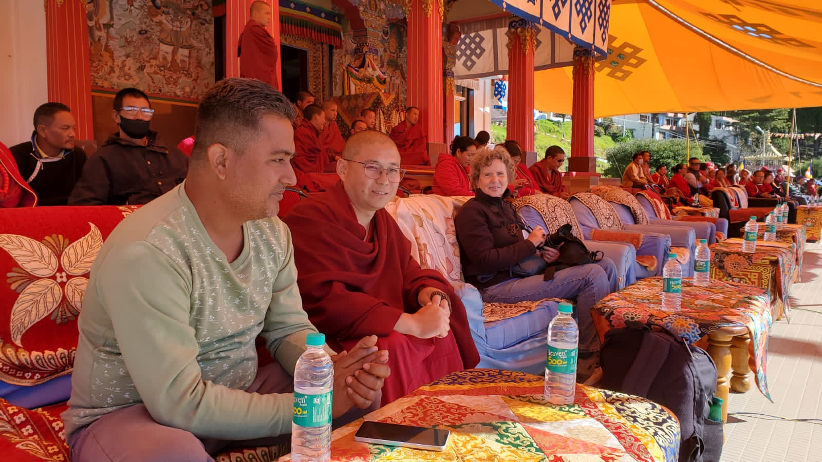 Travellers seated among monks and villagers watching a monastery ceremony in Tawang