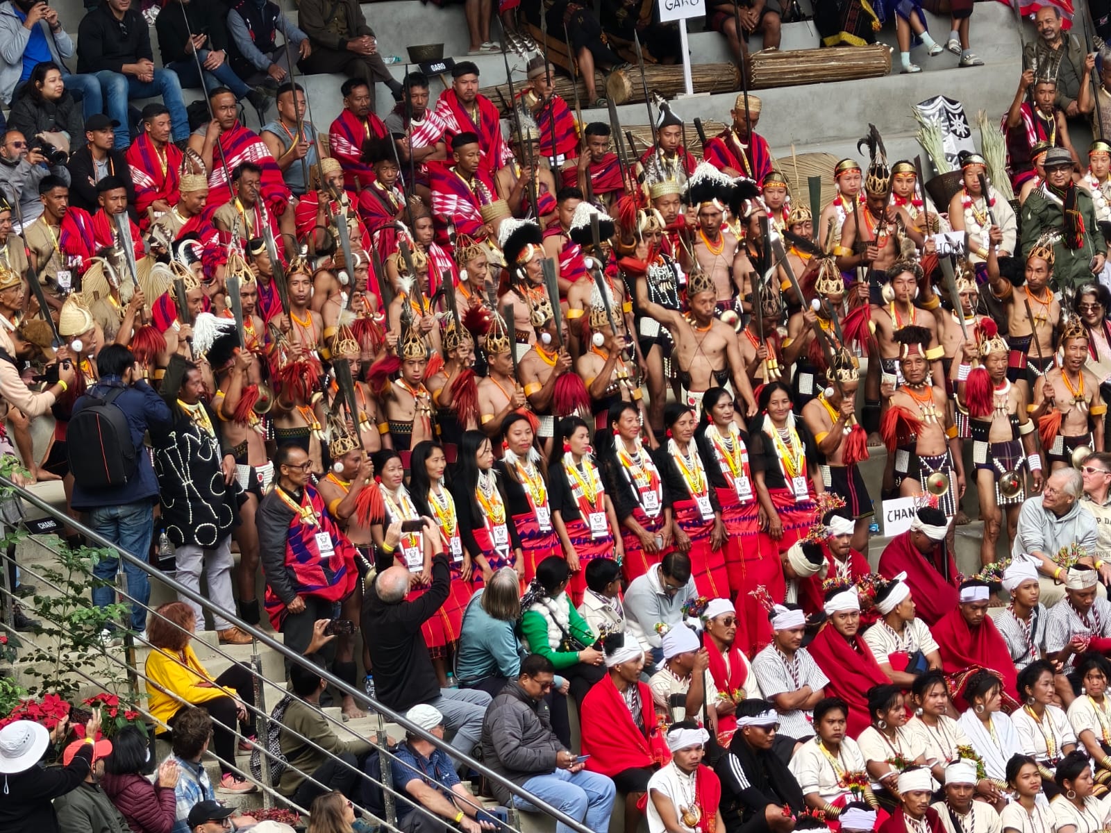 Naga tribal groups in ceremonial dress gathered in the tiered stands around the arena at the Hornbill Festival, Kisama