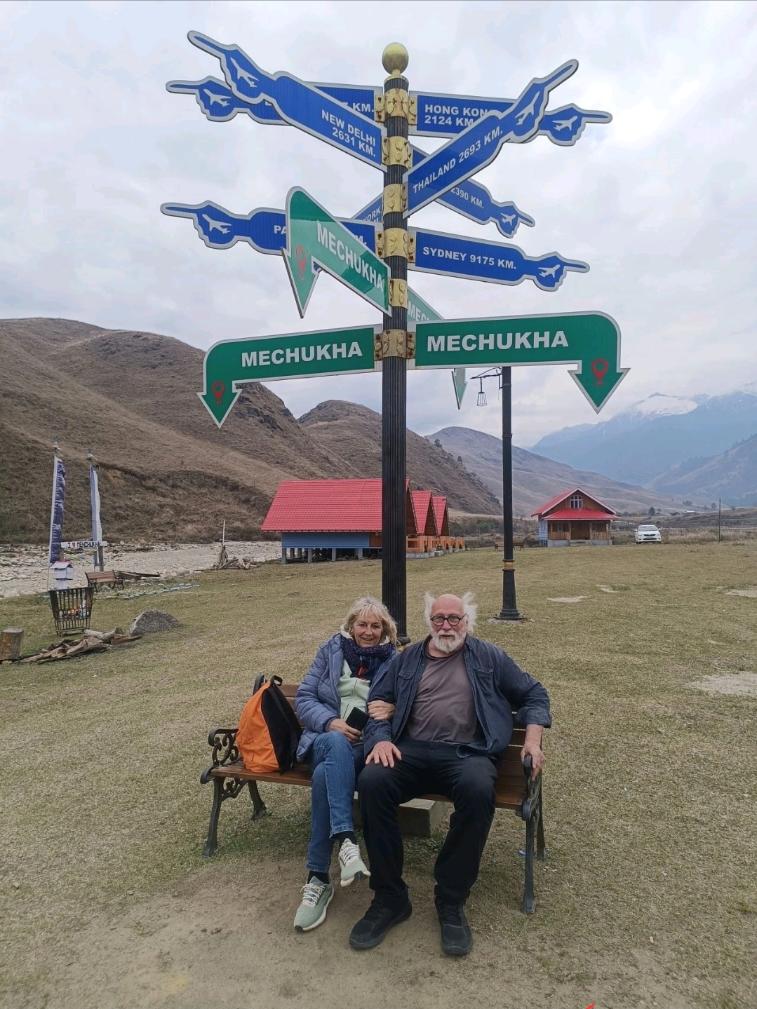 Diminque and Jeans Pierre seated beneath the Mechuka direction sign in Arunachal Pradesh