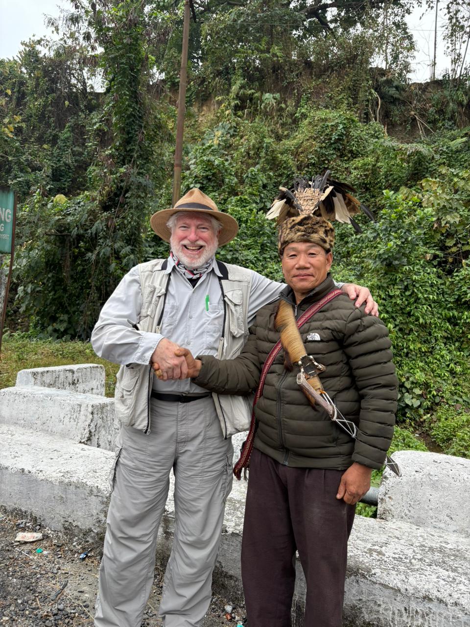 George Lowe shaking hands with a tribal elder wearing a feathered hornbill headdress in Arunachal Pradesh