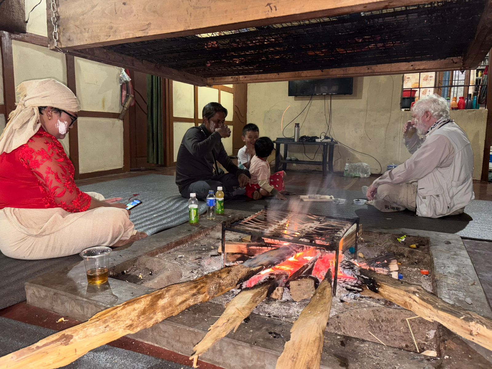 George Lowe drinking tea with a host family beside the hearth fire in Arunachal Pradesh
