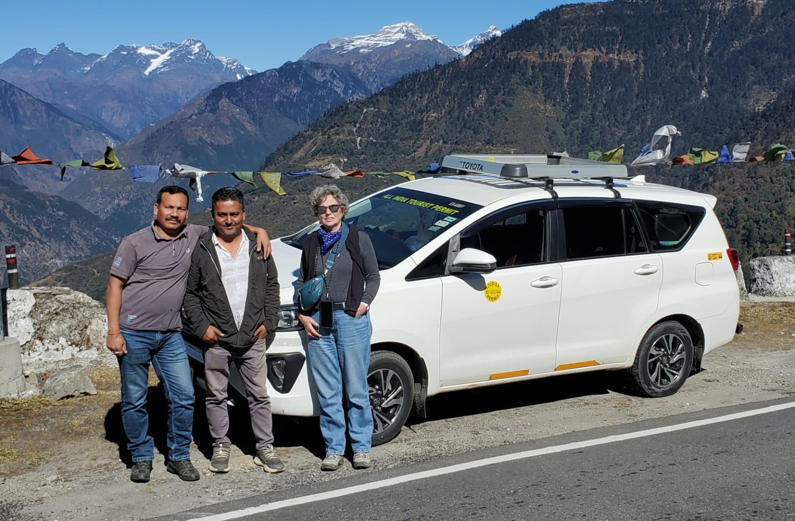 Guide, driver and traveller beside the tour vehicle at a Himalayan viewpoint near Tawang