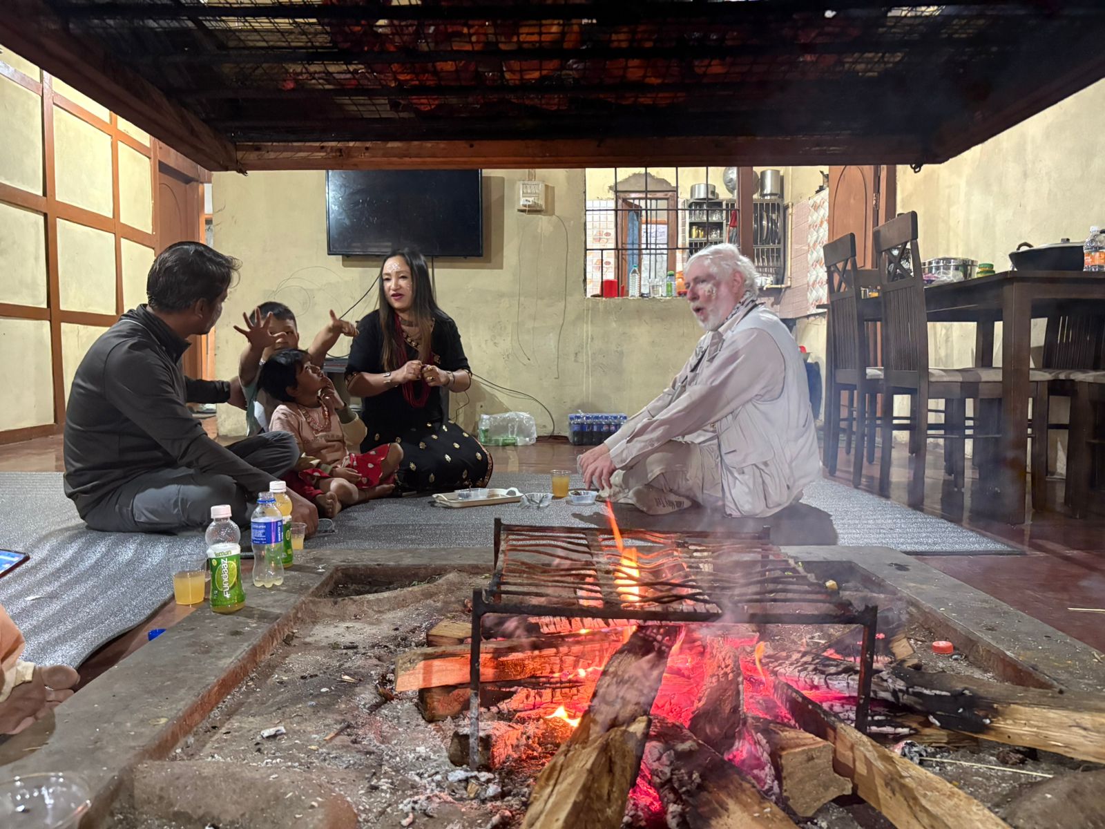 George Lowe seated with a family around an open hearth fire inside an Arunachal Pradesh home
