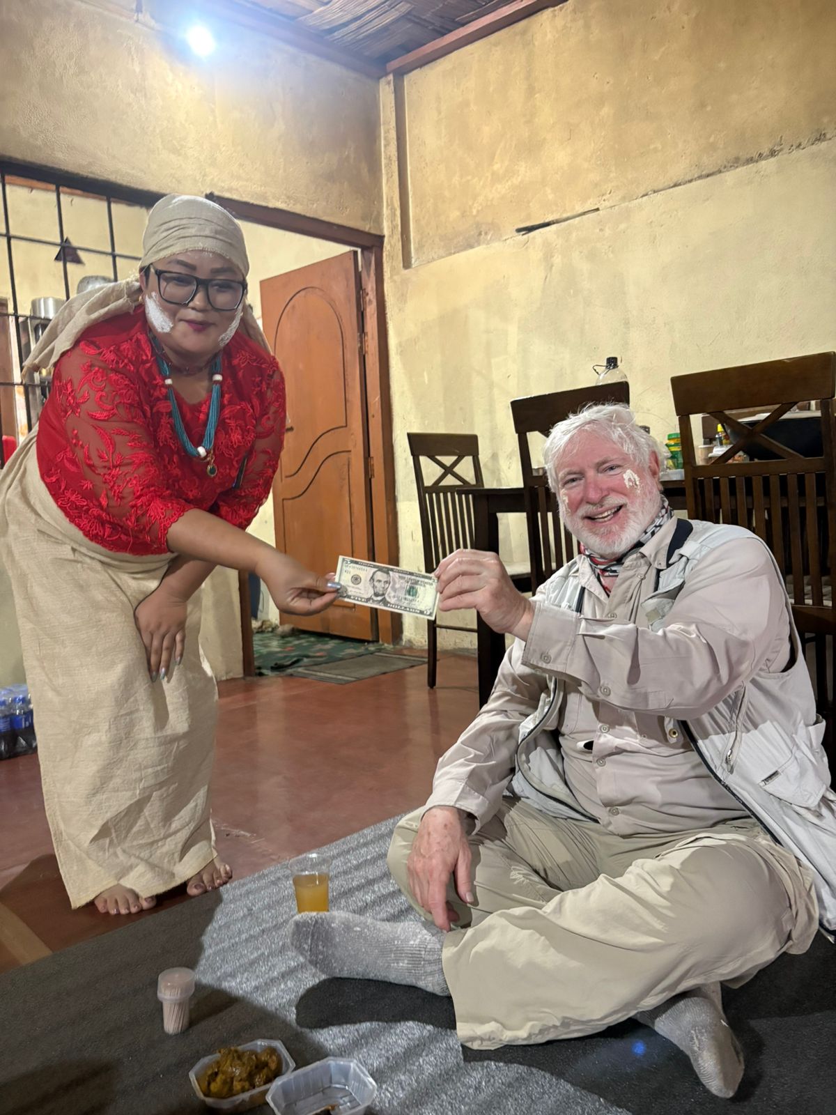 A host in red and cream traditional dress presenting a gift to George Lowe during a village celebration