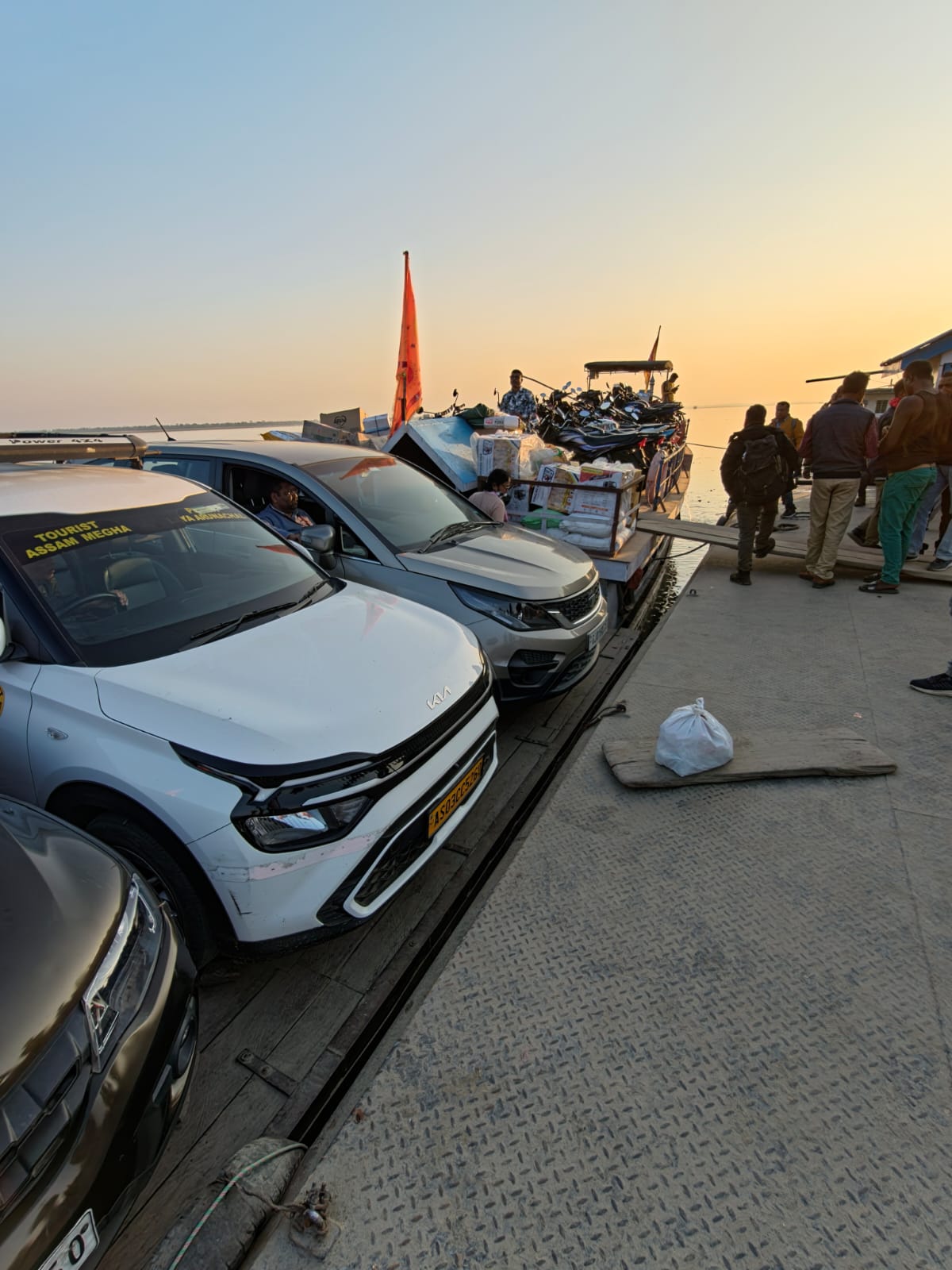 Cars loaded onto a steel ferry crossing the Brahmaputra river at sunset towards Majuli island